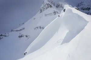 Skier On Crest Of Big Drop, Dwarfed By Mountain; Canada, British Columbia, Icefall Lodge Skier On Crest Of Big Drop, Dwarfed By Mountain; Canada, British Columbia, Icefall Lodge