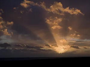 Sunset at sea with partly cloudy sky and sun rays; Brighton, East Sussex, England Sunset at sea with partly cloudy sky and sun rays; Brighton, East Sussex, England