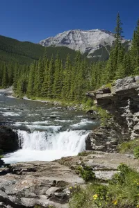 Waterfalls With Rock Ledge And Mountain In The Background; Alberta, Canada Waterfalls With Rock Ledge And Mountain In The Background; Alberta, Canada