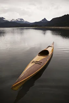 A Wooden Kayak Sits On Tranquil Water With A View Of The Mountains In The Background A Wooden Kayak Sits On Tranquil Water With A View Of The Mountains In The Background