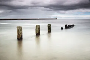 Wooden posts in the ocean with a lighthouse at the end of a pier Wooden posts in the ocean with a lighthouse at the end of a pier