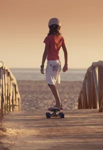 A Young Person Skateboarding With Bare Feet Over A Wooden Boardwalk Towards The Beach; Tarifa, Cadiz, Andalusia, Spain A Young Person Skateboarding With Bare Feet Over A Wooden Boardwalk Towards The Beach; Tarifa, Cadiz, Andalusia, Spain