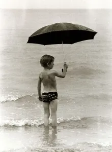 Boy paddling in the sea in the rain holding up an umbrella in Clacton Essex. 1980 Boy paddling in the sea in the rain holding up an umbrella in Clacton Essex. 1980