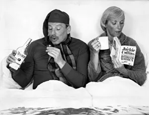 The British at bed time. Husband and wife in bed. He drinks whisky while she reads her The British at bed time. Husband and wife in bed. He drinks whisky while she reads her