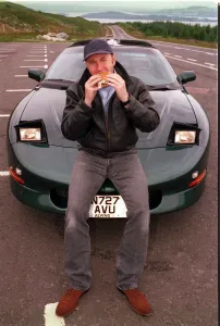 COMEDIAN Fred MacAulay WITH SUPER CAR TRANS AM EATING A HAMBURGER COMEDIAN Fred MacAulay WITH SUPER CAR TRANS AM EATING A HAMBURGER