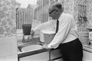 An elderly man running the tap in his kitchen, filling up buckets as a water shortage An elderly man running the tap in his kitchen, filling up buckets as a water shortage