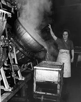 A factory worker tipping a huge cauldron of boiling jam A factory worker tipping a huge cauldron of boiling jam