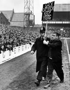 A fan being escorted off the football pitch by a policeman A fan being escorted off the football pitch by a policeman