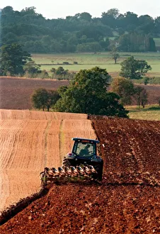 A farm worker steers his tractor and plough in the early evening light on land A farm worker steers his tractor and plough in the early evening light on land