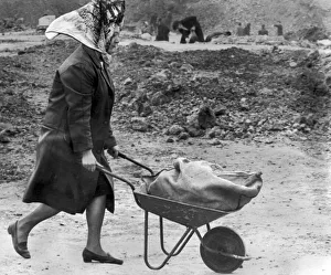 A housewife, cigarette dangling from her lips, nonchalantly wheels away a barrowload of A housewife, cigarette dangling from her lips, nonchalantly wheels away a barrowload of