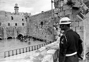An Israeli soldier stands guard while Jewish people worship at the ancient wailing wall An Israeli soldier stands guard while Jewish people worship at the ancient wailing wall