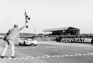 Jim Clark takes the checkered flag in his Lotus 23 to win the Martini Rossi Trophy race Jim Clark takes the checkered flag in his Lotus 23 to win the Martini Rossi Trophy race