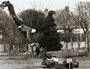 A man mowing his lawn with doing a hand stand on the handles of an electrical lawn mower A man mowing his lawn with doing a hand stand on the handles of an electrical lawn mower