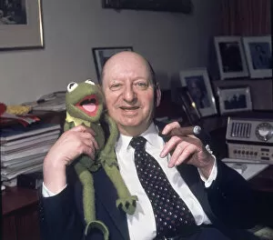 Images Dated 12th March 1978: Media Mogul Lew Grade sitting at his desk smoking a cigar while holding Kermit the frog