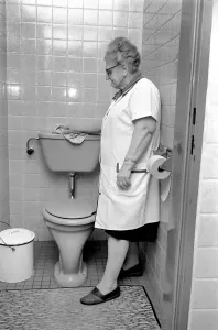 Print of an elderly woman cleaning a toilet, November 1969