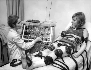 Black and white print of Paula Byrne operating a slimming machine