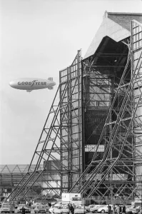 Prints of The Goodyear airship Europa seen here flying past the giant R101 sheds at Cardington, Bedfordshire. 8th March 1972 Bedfordshire Prints: The Goodyear Airship Europa Print: Cardington R101 Sheds