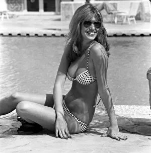 Model wearing a bikini and sunglasses as she sits by the side of a swimming pool in Model wearing a bikini and sunglasses as she sits by the side of a swimming pool in