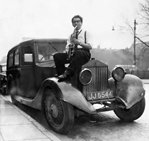 Musician Johnny Roadhouse sitting on the bonnet of a car playing his saxophone Musician Johnny Roadhouse sitting on the bonnet of a car playing his saxophone