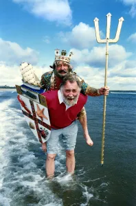Naturalist David Bellamy carries Neptune, alias Mr Phil Lodge out of the surf on the Blue Naturalist David Bellamy carries Neptune, alias Mr Phil Lodge out of the surf on the Blue