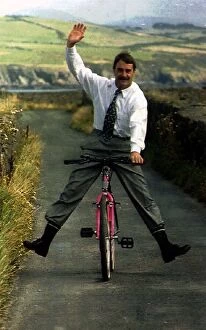 Images Dated 19th August 1992: Nigel Mansell Formula One Racing Driver Riding A Bicycle Down A Country Lane