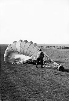 A paratrooper hauling in the parachute attached to a container which has been dropped A paratrooper hauling in the parachute attached to a container which has been dropped