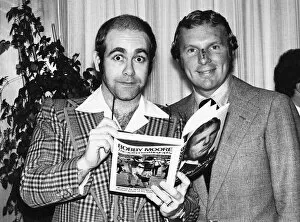Images Dated 26th October 1976: Pop star and chairman of Watford Football Club Elton John helps footballer Bobby Moore