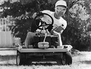 Images Dated 1st June 1978: Stirling Moss sitting on lawn mower wearing crash helmet