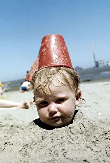 Summer holidays July 1976 - Boy buried in sand with red plastic Bucket on his head Summer holidays July 1976 - Boy buried in sand with red plastic Bucket on his head