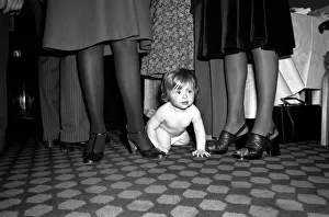A young baby seen here crawling between the legs of adults at a gathering of them parents A young baby seen here crawling between the legs of adults at a gathering of them parents