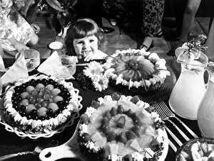A young girl looking at a table with cakes. 1970 A young girl looking at a table with cakes. 1970