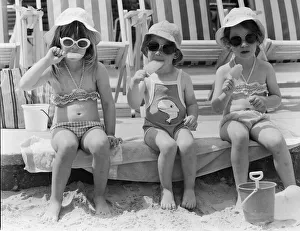 Three young girls sitting on the beach, enjoying an ice lolly. 26th June 1979 Three young girls sitting on the beach, enjoying an ice lolly. 26th June 1979