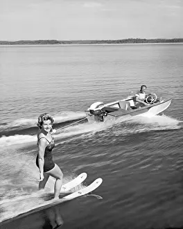 United States: c. 1958 A pretty woman smiles at the camera as she holds on with one hand while water skiing on a lake