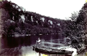 Mountain River Scenery Prints: A stretch of river surrounded by mountains. In the foreground a rowboat and its owner