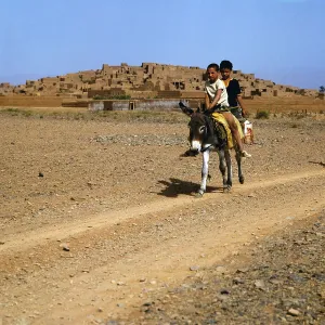 Marokko Print: Two Boys on a Donkey before a Small Town near the Sahara
