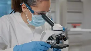 Microscope Laboratory Equipment Prints: Biologist with face mask using microscope in science laboratory