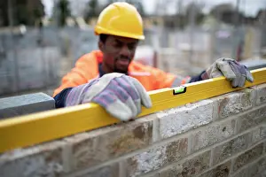 Building Site Safety Prints: Male construction worker using level tool on brick wall