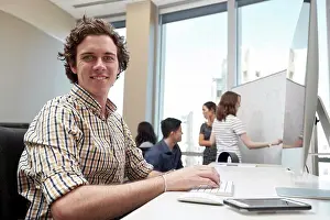 Office Communication Skills Prints: Young man using computer in office looking towards camera