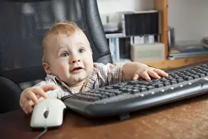 Young Boy At Desk Prints: Boy, 10 months, using a computer mouse and keyboard