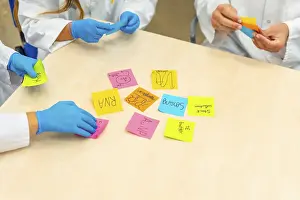 Young Adults In Healthcare Prints: Close-up photo of group of scientists during a brainstorm study using notes in lab