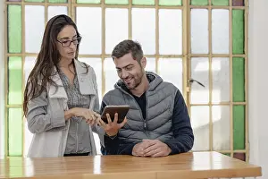 Office Collaboration Prints: Two colleagues discuss while using a tablet in a bright office