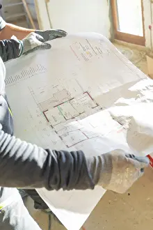 Interior Architecture Prints: A construction worker holds a construction plan in his hands in a light-filled room