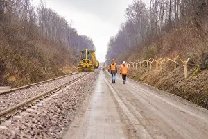 Railway Construction Site Prints: Construction worker and machine tool working on a railroad track in the forest