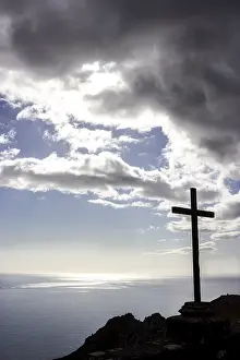 Uninhabited Rocky Shore Prints: Cross on a cliff with storm clouds