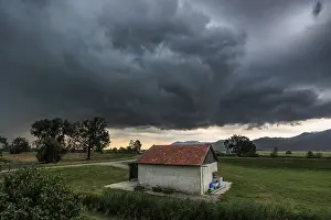 Stormy Atmosphere In Europe Prints: Dark storm clouds over a small barn