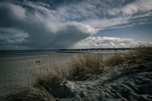 German Federal Republic Coastal Scenery Prints: Dramatic cloud formations over a beach with a long pier in the background
