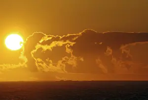 Atmospheric Light Of The Setting Sun Prints: A dramatic sunset over the sea with bright orange clouds