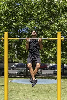 Recreational Activity Outdoors Prints: Fit young man executing pull-ups in a park setting