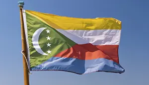 Prints of The flag of the Comoros flutters in the wind, isolated against a blue sky Comoros Prints: The Flag of Comoros Print: A Blue Sky Scene