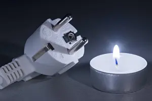 Power Failure Concept Prints: Glowing candle next to electrical plug in cold light